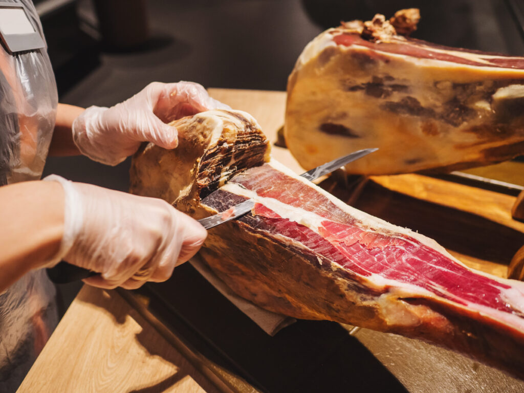 Persona cortando jamón ibérico con cuchillo jamonero mostrando la textura y calidad de la pieza