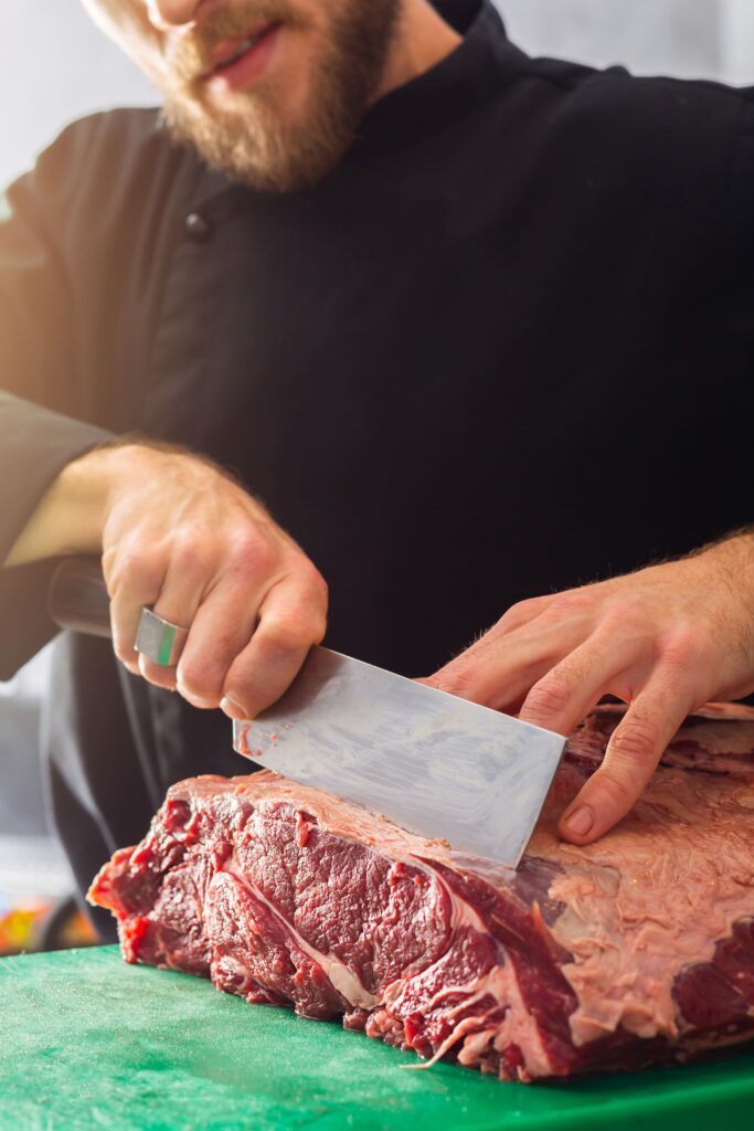 Chef porcionando corte de carne de vacuno en cocina profesional — distribuidor de carne para hostelería en Murcia